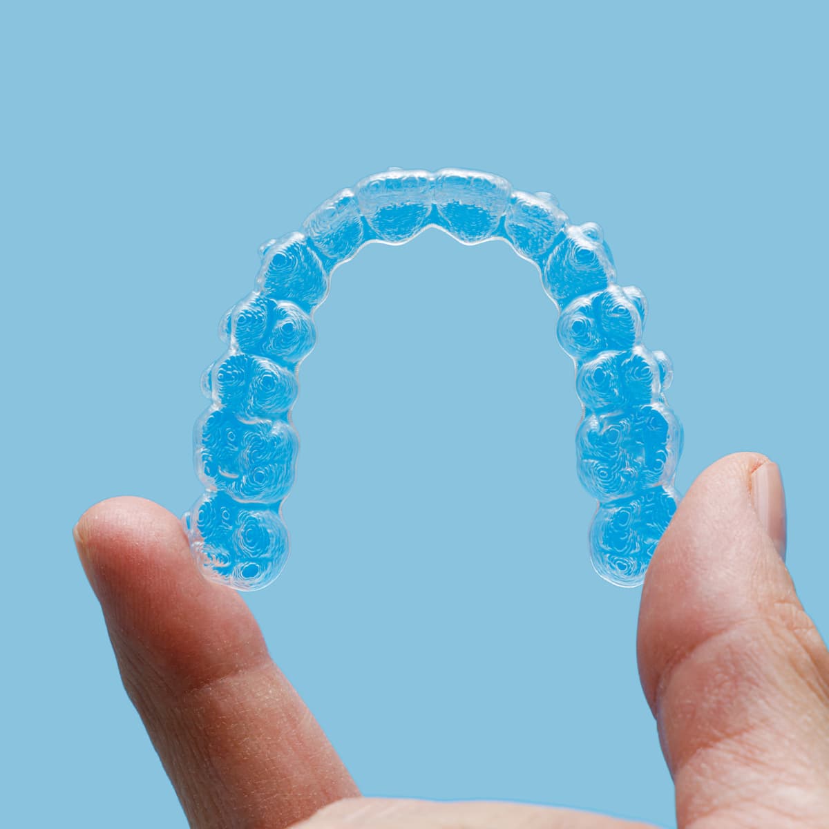 Alineador dental transparente sostenido con los dedos